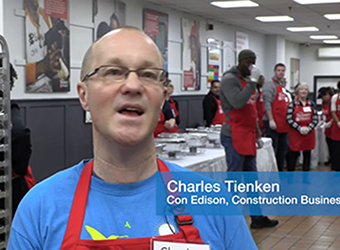 A Con Edison volunteer standing in front of food serving stations.