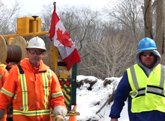 a Canadian Mutual Aid utility worker and a Con Edison worker on a snowy worksite with Canadian flag in the background