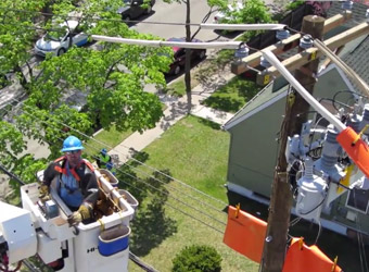 A Con Edison is using a bucket truck to reach overhead power lines.