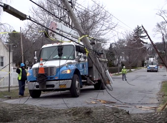 Utility truck and workers securing broken telephone poles that are broken and knocked over in the street with wires down.