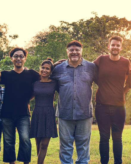 A group of people are standing arm-in-arm outside in a field or park. 